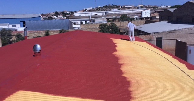 Dos técnicos proyectando espuma de poliuretano sobre un techo de chapa mini-onda y aplicando pintura de caucho de exterior roja