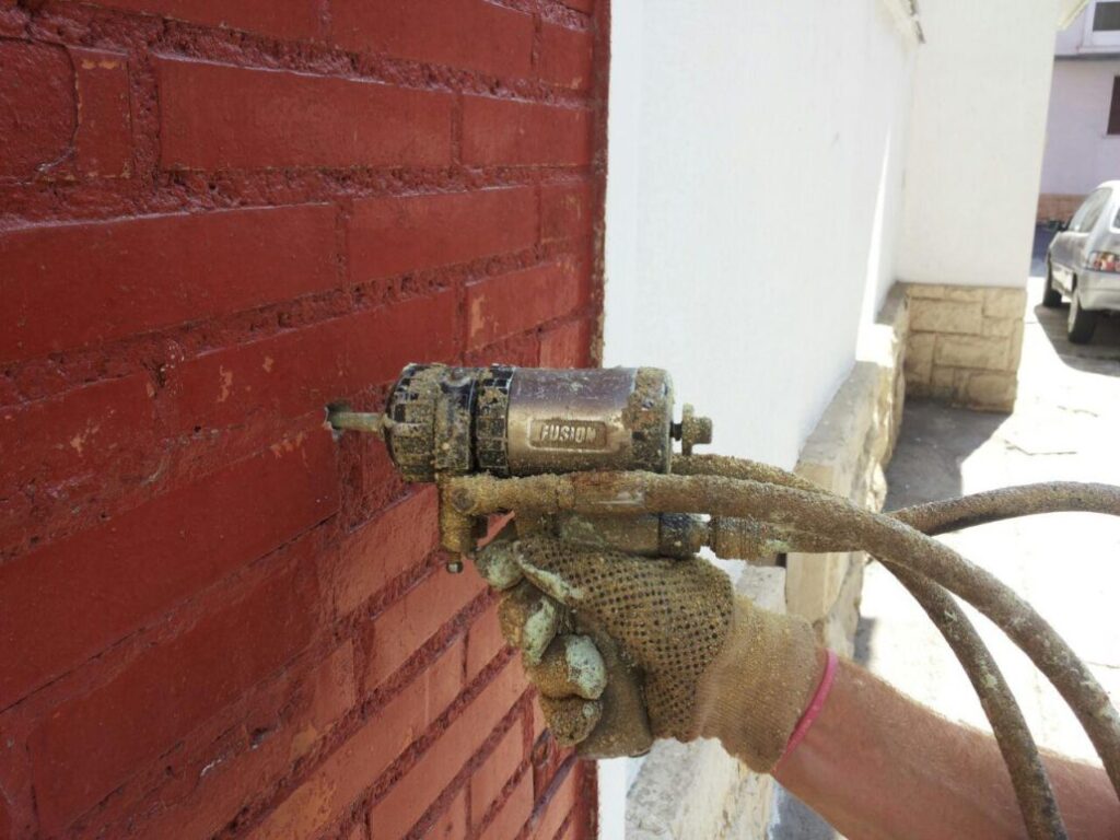 Persona inyectando espuma de poliuretano dentro de una cámara con una pistola de aislamiento de poliuretano a través de un agujero en la pared. Inyección Poliuretano en Cámaras